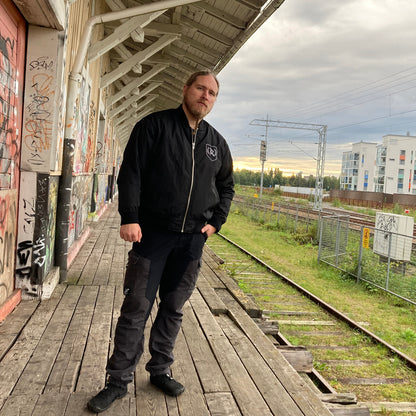 Rurik Fightgear-lentäjänpusakka.
Rurik FG "R" -logo rintapielessä sekä riimulogo selässä monivärisesti brodeerattuna. Kuvassa pilottitakki  Mikan päällä junan laiturilla. PT-Combat.Fi
