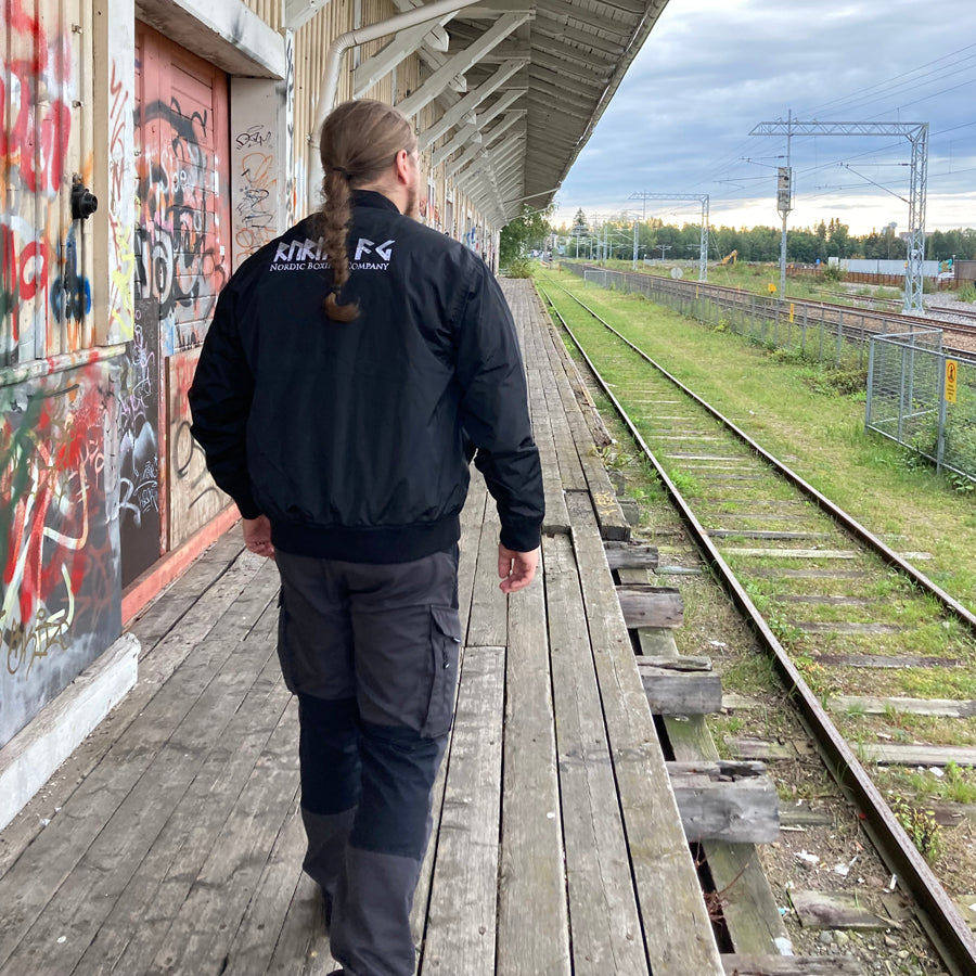 Rurik Fightgear-lentäjänpusakka.
Rurik FG "R" -logo rintapielessä sekä riimulogo selässä monivärisesti brodeerattuna. Kuvassa pilottitakki  Mikan päällä takaa kuvattuna. PT-Combat.Fi